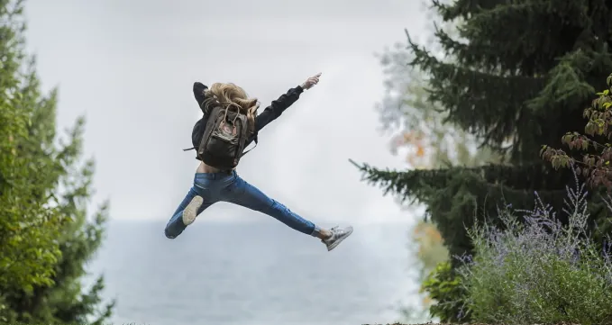 Eine Person springt mit ausgestreckten Gliedmaßen in die Luft zwischen Bäumen.