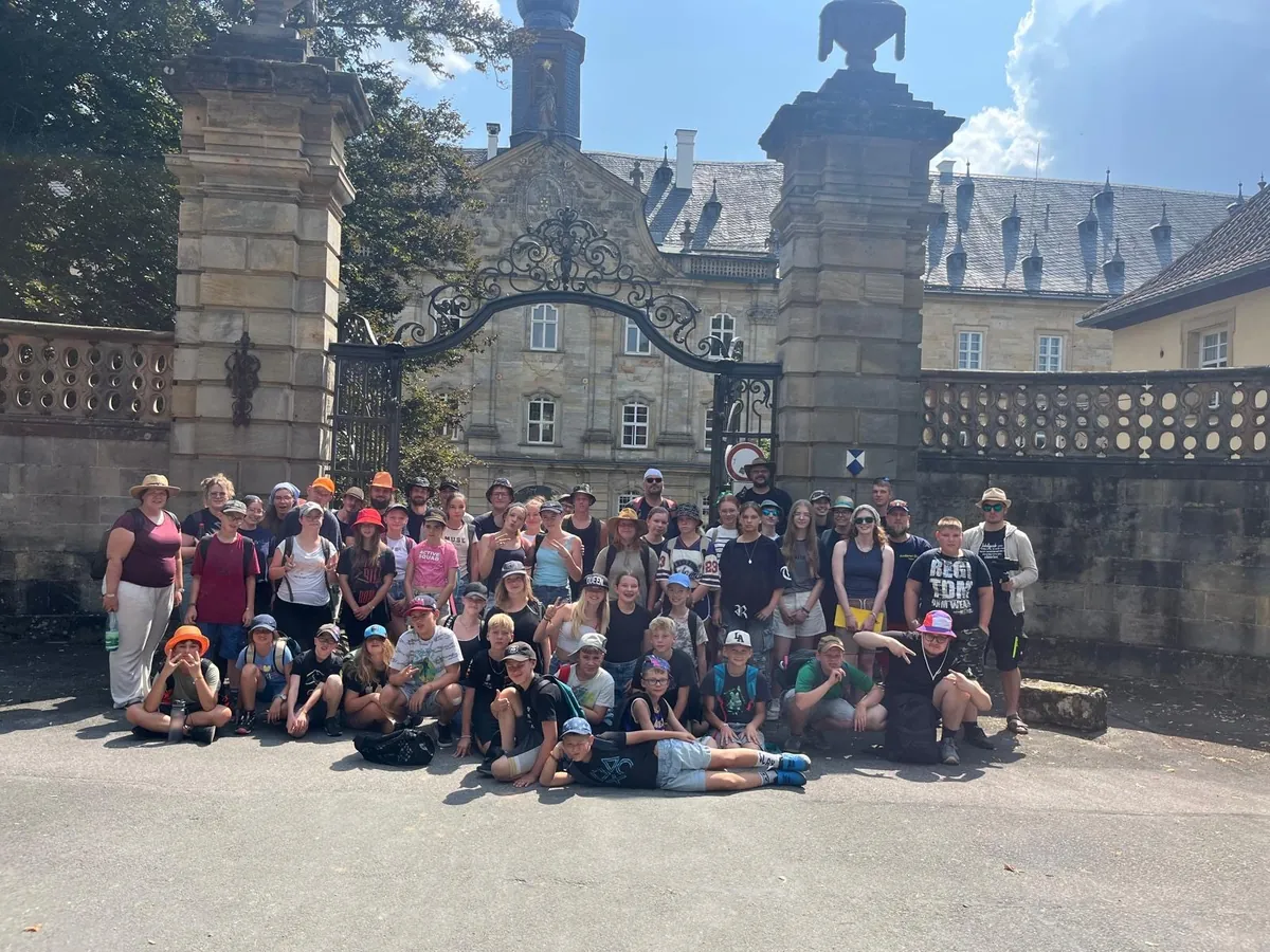 Rund 45 Kinder und 20 Teammitglieder stehen vor dem großen Tor vom Wildpark Schloss Tambach für ein Gruppenfoto zusammen.
